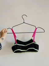 Conjunto de dos piezas compuesto por un top y una bombacha. El top es negro con ribetes en color verde claro y tirantes fucsias. La bombacha es negra con detalles en verde claro.