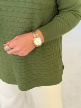 Sweater de punto color verde oliva con diseño de trenzas horizontales, cuello redondo y mangas largas con puños acanalados. Presenta un corte holgado con aberturas laterales en el ruedo.