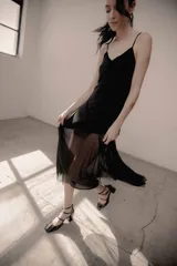 Vestido midi negro con tirantes finos, escote en V y detalles de terciopelo. Cuenta con una sobrecapa de microtul transparente en la parte inferior que aporta movimiento y ligereza.
