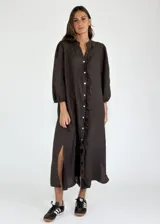 Vestido largo color beige de lino, con cuello mao, mangas 3/4 abullonadas y cierre frontal con botones. Presenta volantes verticales en el frente.