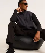 Chaleco deportivo gris oscuro con cuello alto y cierre frontal con cremallera. Presenta recortes en tejido liso en la parte superior del pecho y en los bolsillos laterales.