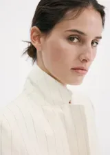Blazer corto de mezcla de lino en color beige con rayas sutiles, de corte recto, cuello con solapa de muesca, mangas tres cuartos, cierre frontal de un botón y bolsillos con solapa.