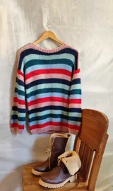 Buzo de punto tejido a mano con lana merino, con diseño de rayas horizontales multicolor en tonos rosado, azul marino, verde y rojo.