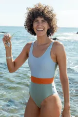 Malla enteriza con diseño tricolor en bloques, presentando un panel superior celeste, una franja central naranja y un panel inferior verde. Posee escote redondo y breteles anchos.