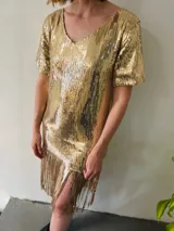 Vestido corto dorado de lentejuelas con escote en V, mangas cortas y flecos en el ruedo.