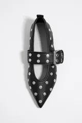 Bailarinas negras de cuero con punta fina, tachas plateadas y correa con hebilla metálica. Zapato plano con suela fina.