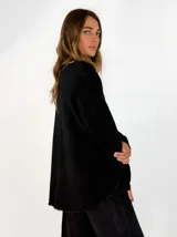 Sweater de punto gris con cuello redondo, mangas largas y diseño asimétrico, siendo más corto en la parte delantera y más largo en la trasera, con detalles de terminación en contraste.