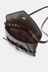 Bolso formato bandolera de material sintético con acabado metálico plateado. Presenta un diseño de solapa frontal con un cinturón decorativo que se cierra con una hebilla metálica en forma de corazón. Incluye un asa bandolera fina de cadena y un bolsillo interior con cierre.