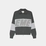 Campera de tejido de punto gris oscuro con cierre frontal y cuello polo. Presenta un diseño de bloques de color con franjas horizontales grises claras en el pecho y mangas. La palabra "EME" está tejida en letras grandes en el centro del pecho.