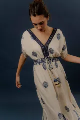 Vestido largo beige con estampado paisley en color azul marino, escote en V profundo con detalle bordado, mangas cortas amplias, cordón ajustable en la cintura con borlas y volados en el ruedo.