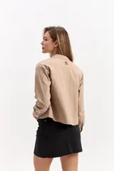 Chaqueta liviana color beige, de corte recto, con cuello camisero, cierre frontal con broches y bolsillos aplicados.