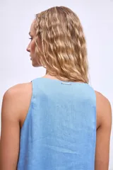 Vestido corto blanco sin mangas, con escote en V y detalle de broche dorado en el centro. La falda tiene un volado en el ruedo.