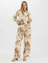 Conjunto de dos piezas compuesto por camisa de manga larga con cuello solapa y botones frontales, y pantalón de tiro alto con pierna recta y bolsillos laterales. Ambas prendas presentan un estampado paisajístico en tonos marrones sobre fondo crema.