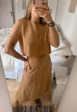 Conjunto de dos piezas compuesto por un top corto sin mangas y una pollera larga con tajo lateral. El top presenta un diseño minimalista y la pollera es ajustable en la cintura.