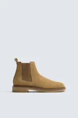 Bota estilo Chelsea de hombre, color marrón, fabricada en piel con acabado serraje (gamuza). Presenta elásticos laterales oscuros y suela de goma a tono con tacón bajo.