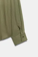 Camisa verde militar confeccionada en mezcla de lino, con cuello solapa, escote en pico, manga larga y diseño asimétrico con pliegues en la parte delantera.