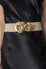Cinturón elástico de color crudo con hebilla metálica dorada en forma de dos flores entrelazadas.