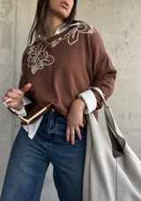 Sweater de punto color chocolate, de corte holgado, manga larga y cuello redondo con delicados bordados contrastantes en el frente.