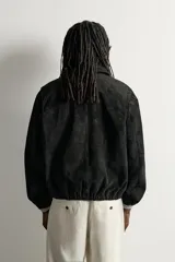 Cazadora de piel con acabado serraje de corte relaxed fit, color negro, con cuello solapa, bolsillos de vivo en la cadera, bajo elástico y cierre frontal con cremallera de doble dirección. Colección especial Aaron Levine x ZARA.