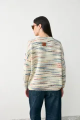 Sweater de punto con diseño oversize y cuello en V, tejido en tonos crudo con rayas horizontales multicolores.