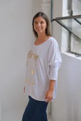 Remera blanca de corte holgado y manga larga, con estampado floral en color dorado en el frente.