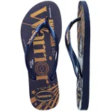 Ojotas Havaianas modelo Slim, color azul marino con estampa dorada y gris de Wonder Woman. La ojota izquierda muestra la palabra "Wonder Woman" y la derecha presenta un retrato del personaje con fondo de rayos dorados y estrellas.