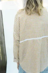 Camisa de manga larga con estampado vichy en color mostaza y blanco, cuello mao y apliques de encaje en la pechera. Diseño holgado con cierre frontal de botones y mangas con puños elásticos.