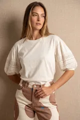 Remera de algodón color crudo con cuello redondo y mangas abullonadas de largo 3/4. Las mangas presentan detalles de encaje bordado y perforado con terminación elástica.