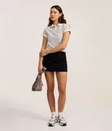 Minifalda de jeans negra, de tiro alto, con cierre tradicional y trabillas en la cintura. Presenta detalles de tachuelas metálicas en los bolsillos delanteros.