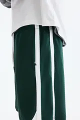 Short deportivo de color verde oscuro, confeccionado en nylon, con bandas laterales blancas, cintura elástica ajustable mediante cordón blanco y corte estándar.