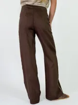 Pantalón marrón de lino de corte recto y holgado, con costuras decorativas claras a lo largo de las piernas.