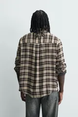 Camisa de corte relajado con diseño de cuadros en tonos negro y beige, cuello camisero, manga larga y cierre frontal de botones.