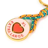 Llavero con dije circular metálico color dorado, esmaltado en rosa con un corazón central y la inscripción 'EXTRA LARGE'. Incluye una argolla y un gancho mosquetón dorados, unidos por cordones trenzados en tonos naranja, turquesa y amarillo.