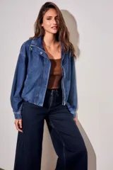 Campera bomber de jean con corte oversize, cierre frontal y cuello alto con botones a presión. Presenta mangas amplias y puños ajustados.