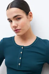 Remera verde de tejido canalé con cuello redondo y media manga. Tiene una abertura frontal con botones.