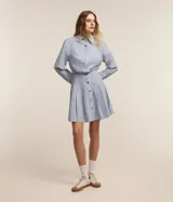 Vestido corto chemise de algodón con estampa a rayas celestes y blancas, cuello solapa, manga larga, abotonado frontal y cintura marcada con falda evasé con pliegues.