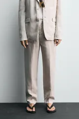 Pantalón de traje regular fit confeccionado en tejido de lino, con bolsillos laterales y bolsillos traseros de vivo con botón. Presenta cierre frontal con cremallera y botón.