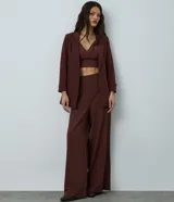 Blazer de sastrería color bordó, de corte oversized y largo, confeccionado en crepé. Presenta solapas clásicas, bolsillos frontales y detalle de pliegues en los puños.