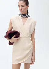 Vestido corto color crema, con escote en V cruzado, sin mangas y falda cruzada con drapeado lateral.
