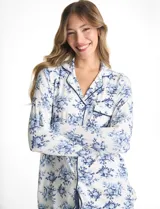 Conjunto de pijama compuesto por una camisa de manga larga con cuello solapa, escote en V, cierre frontal con botones y bolsillo aplicado, junto con un pantalón de cintura elastizada con lazo de ajuste. Presenta un estampado floral en tonos azules sobre fondo blanco.