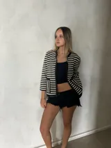 Chaqueta tejida en lana merino a rayas horizontales blancas y negras, con ribete de cuero negro en cuello, cierre y bolsillos.