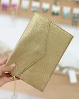 Sobre de fiesta rectangular color dorado con textura lineal y solapa en forma de sobre. Incluye cierre lateral y correa de mano.