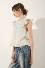 Camisa sin mangas color blanco roto, con volados en los hombros y bordado estilo calado en el frente con motivos florales en hilo celeste.