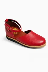 Zapato tipo bailarina o guillermina de cuero rojo texturizado, con punta redonda y tira de tobillo ajustable con hebilla metálica dorada. Suela plana de goma en color negro y beige.