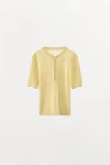 Camiseta de punto en mezcla de algodón color amarillo pastel, con cuello redondo, manga corta y cierre frontal parcial con botones.