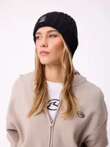 Gorro tipo beanie de punto acanalado en color lila, con parche rectangular negro en el frente que incluye la inscripción 'EAT THE WAVE'.