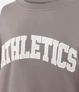 Buzo deportivo de corte oversized color gris topo, con cuello redondo, mangas largas y puños con detalle de rayas blancas. Presenta estampado frontal con la palabra Athletics y ruedo con franja blanca contrastante.
