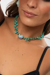 Collar corto estilo choker compuesto por piedras turquesas irregulares y abalorios marrones, con un dije central de cerámica en forma de caracol marino.