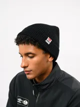Gorro tipo beanie de punto acanalado en color negro, con vuelta y etiqueta de la marca Umbro cosida en el lateral.