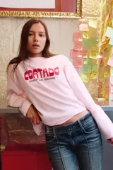Remera de manga larga con hombros caídos y cuello redondo, confeccionada en algodón. Presenta un estampado frontal con el texto 'CORTADO' y una dirección en París, además de un pequeño detalle gráfico en el puño.